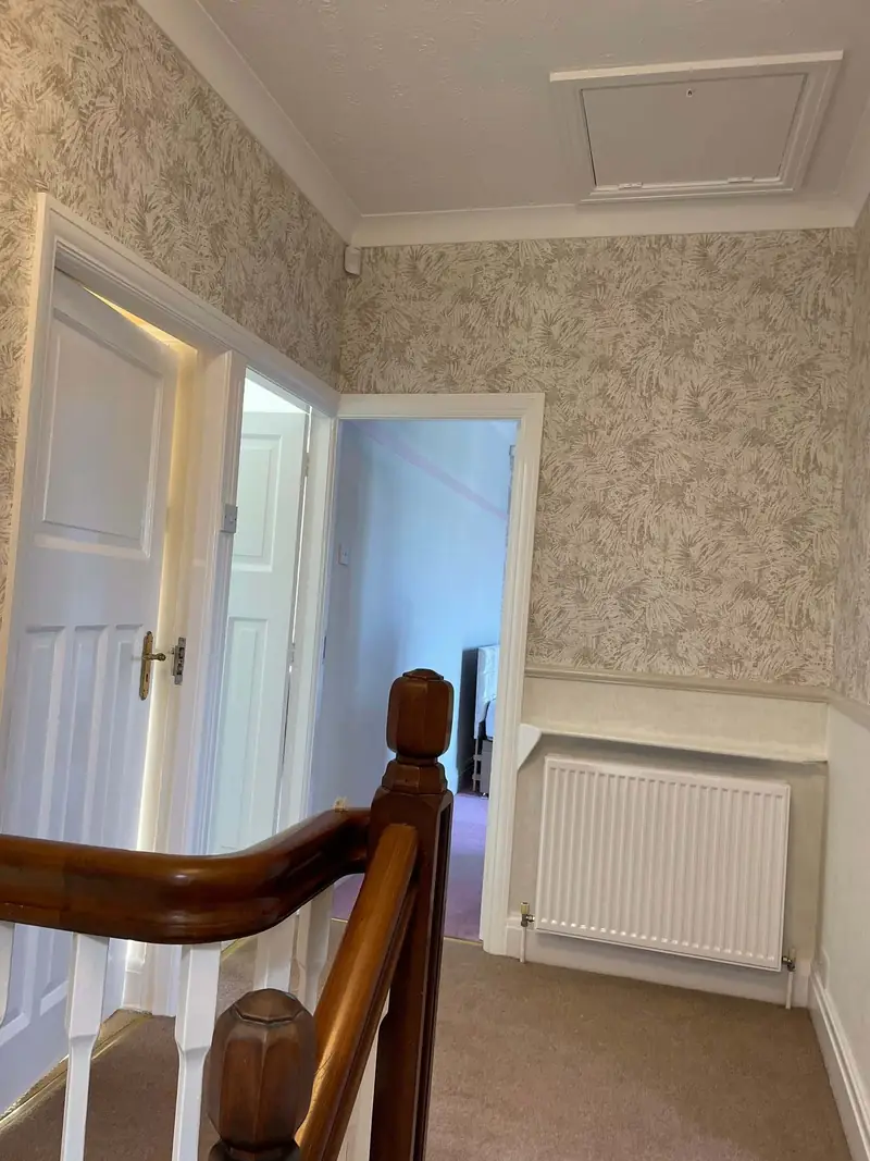 Landing papered in fern-print wallpaper above a white dado, with white panelled doors and a mahogany newel post