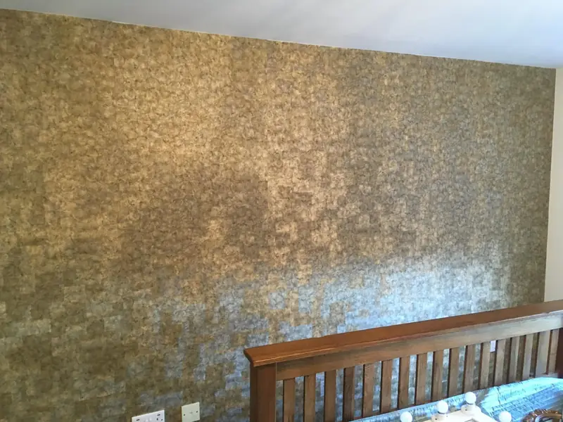 Landing wall papered in a gold and grey textured wallpaper above a wooden bannister