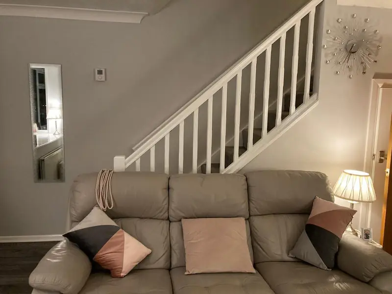 Living room painted soft grey with an open staircase of white spindles and a cream leather sofa